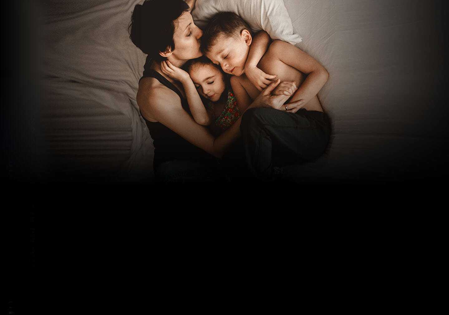 Mãe abraçando o filho e a filha na cama